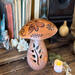 This shows a handmade mushroom decoration. Made from a gourd, it has a fern carved in the stock and wood burned bee artwork on top. 